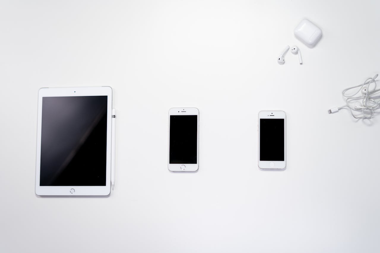 Flat lay of smartphone, tablet, and earphones arranged on a white surface for a clean, minimalist aesthetic.